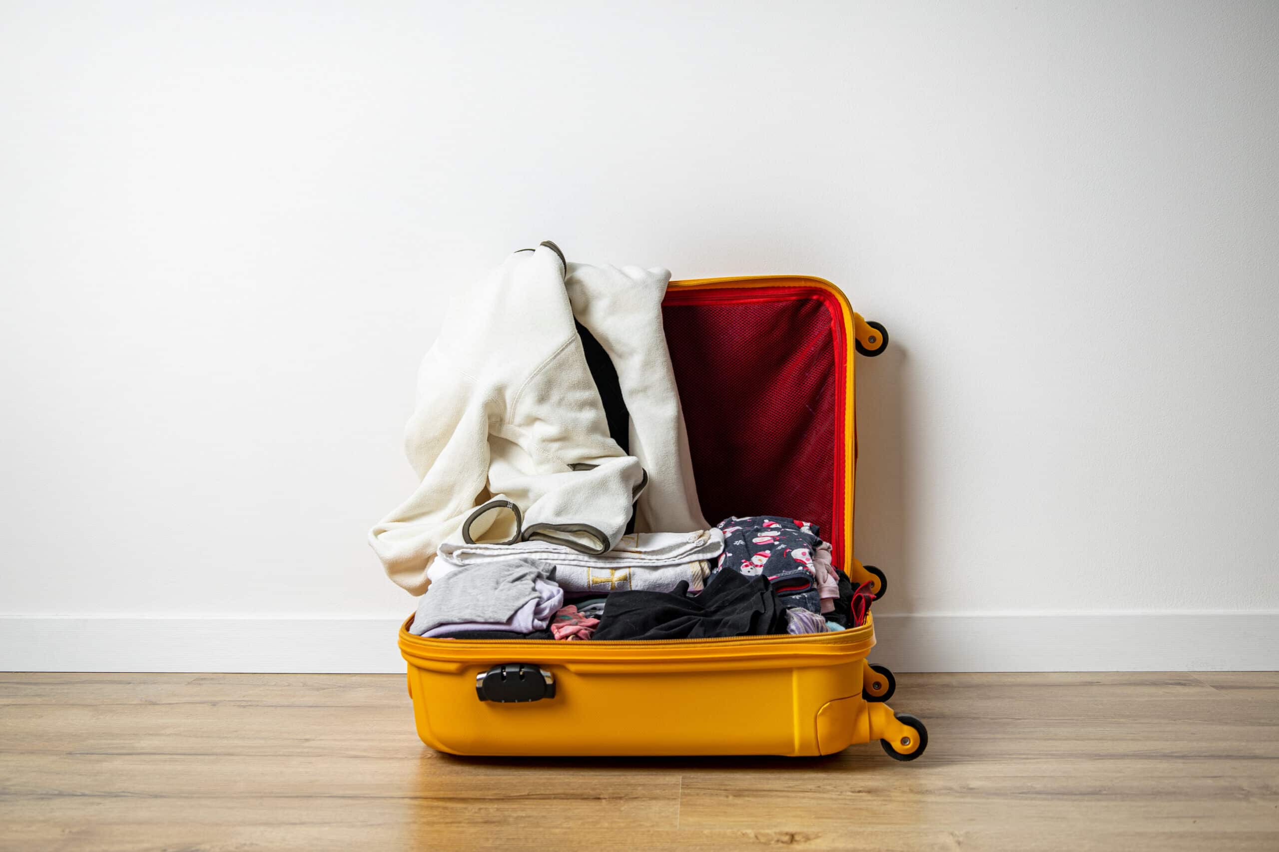 How to Keep Luggage & Clothes Smelling Fresh When Traveling - Open yellow suitcase with clothes on a wooden floor against a white wall