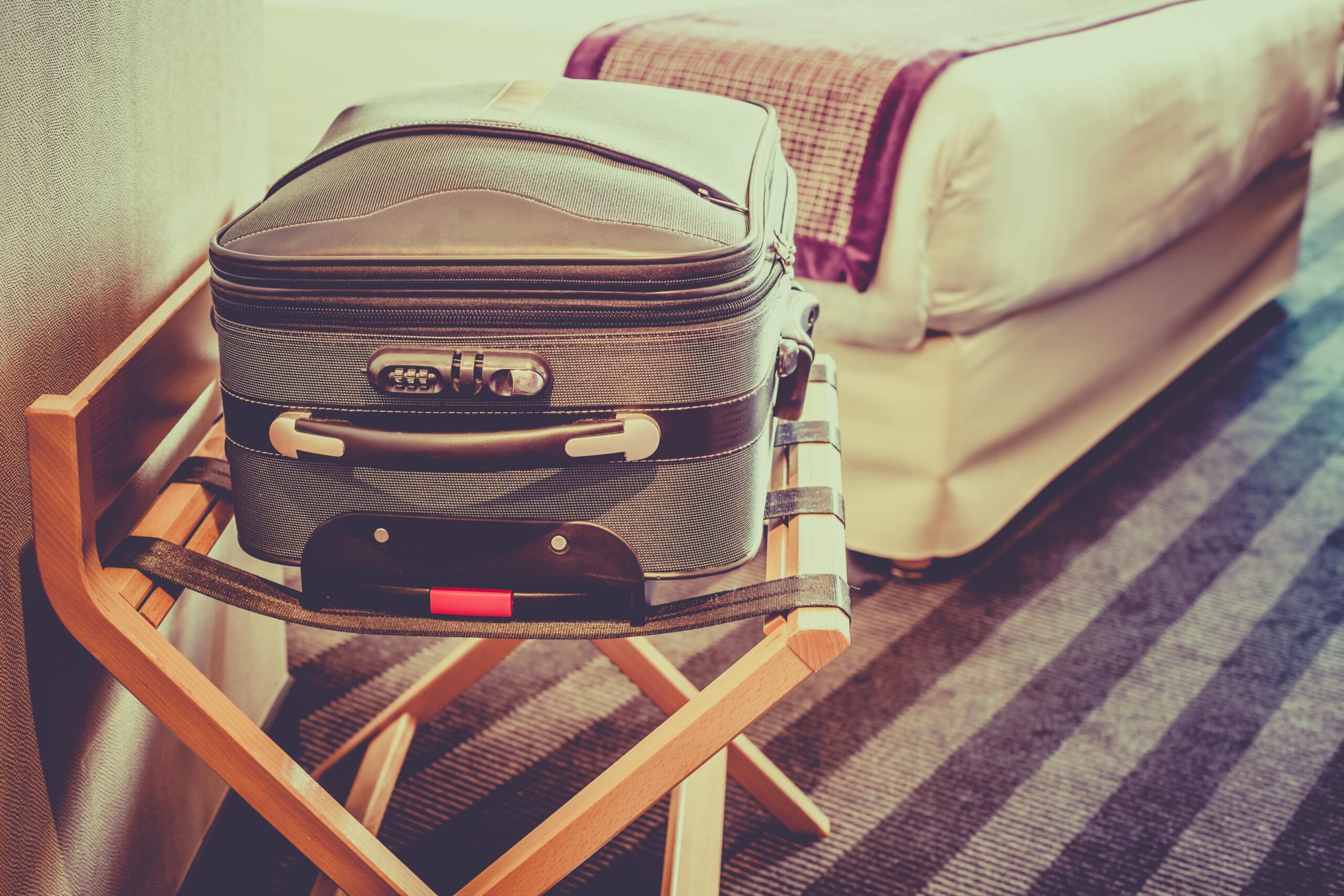 Suitcase on the luggage rack in a hotel room with a bed in the background.
