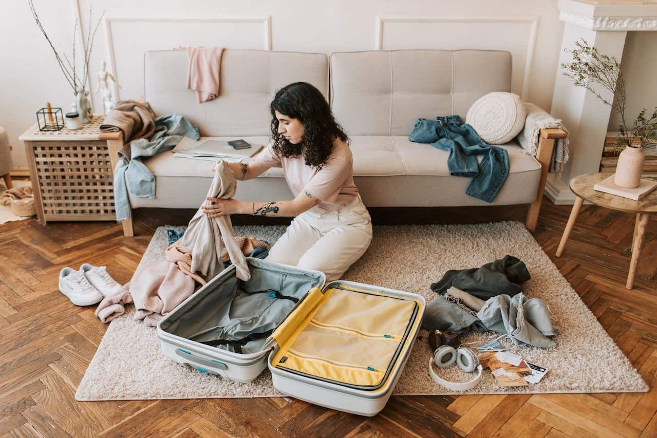 Woman packing suitcase in living room with sofa in the background.