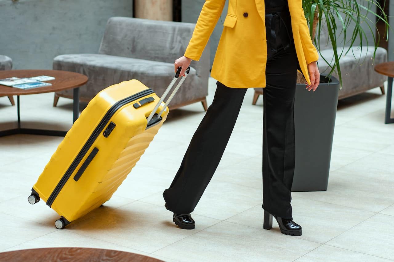 woman with yellow jacket and black pants pulling large yellow suitcase