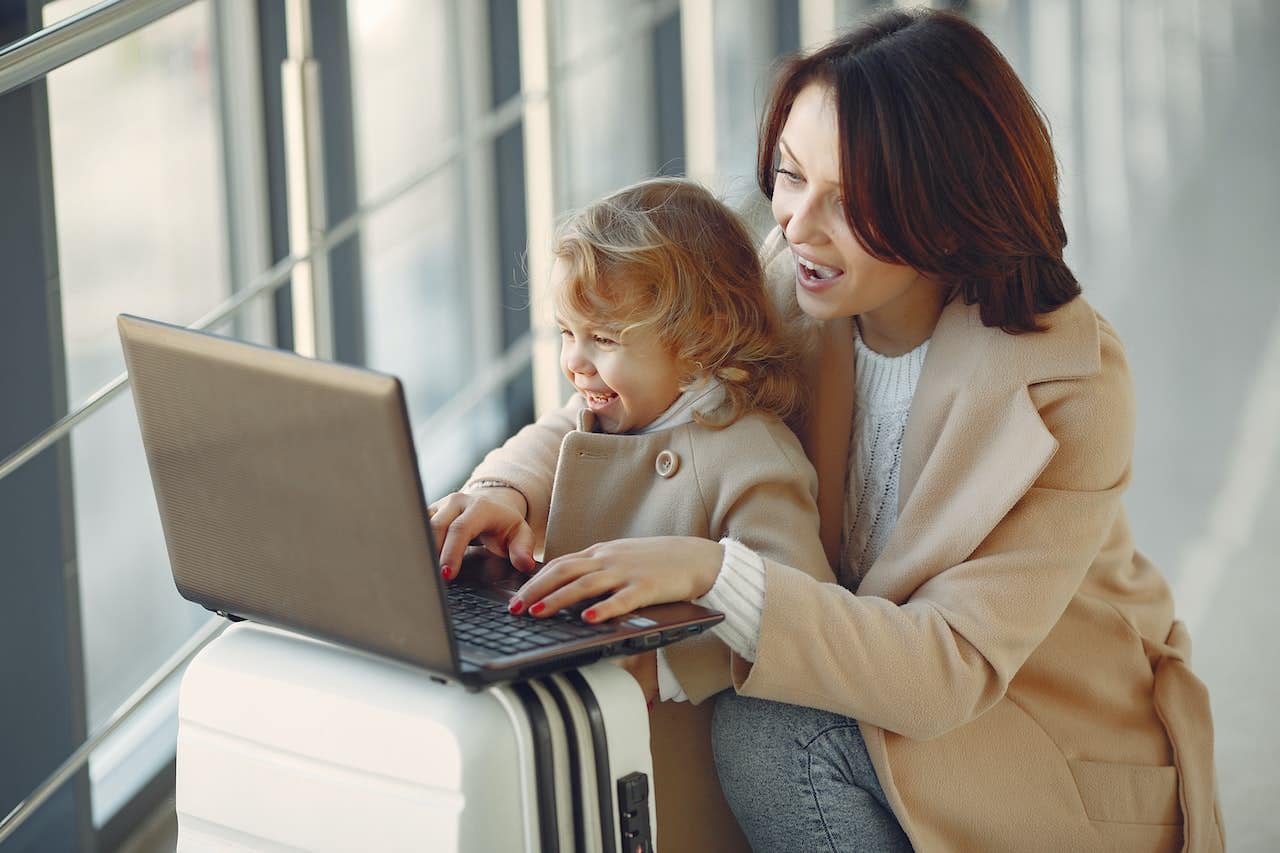 mother and daughter using laptop on luggage at airport