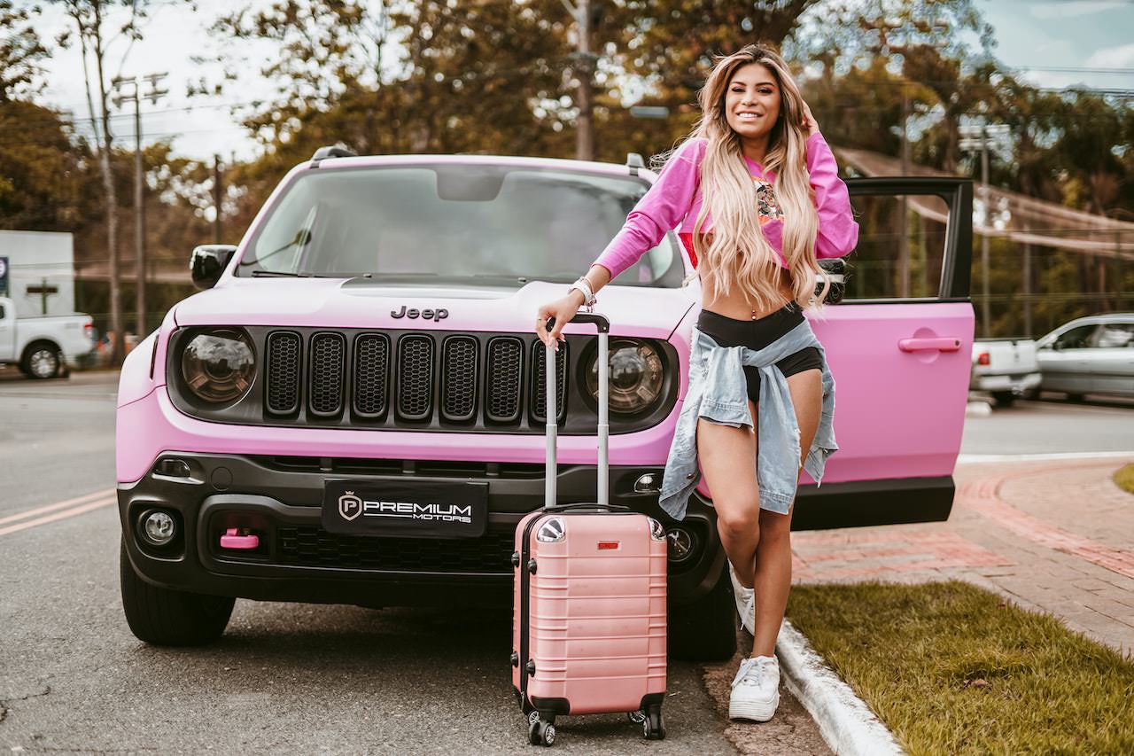 woman with 4-wheel pink carry-on suitcase in front of pink Jeep