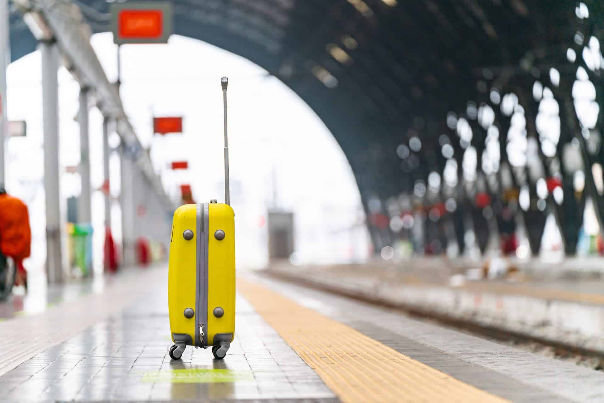 Best luggage for European travel. Yellow suitcase at train station.